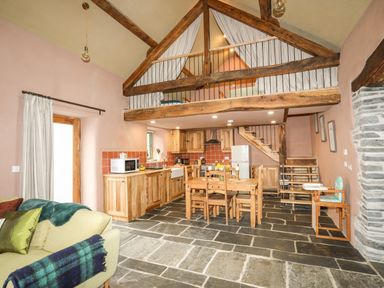 A kitchen and dining area with wooden cabinets and table under a loft with a bed at Tyn Llwyn Cornel Eco Barn in Garreg