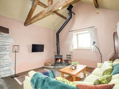 A living room with a wood burning stove wooden coffee table sofa and exposed wooden beams at Tyn Llwyn Cornel Eco Barn in Garreg