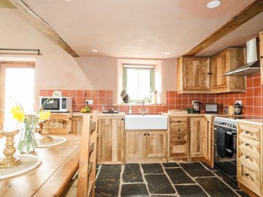 A kitchen with wooden cabinets stone floor and orange tiled backsplash at Tyn Llwyn Cornel Eco Barn in Garreg