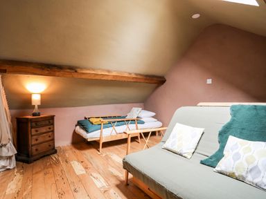 An attic bedroom with a small bed, wooden chest of drawers with lamp, and a sofa with cushions at Tyn Llwyn Cornel Eco Barn in Garreg