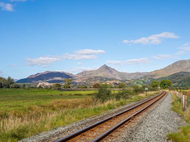 A single railway track running through grassy fields with mountains in the background at Tyn Llwyn Cornel Eco Barn in Garreg