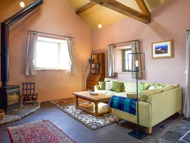 A living room with a wood stove a sectional sofa and a wooden coffee table at Tyn Llwyn Cornel Eco Barn in Garreg
