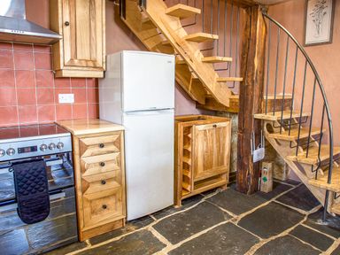 A kitchen area with a stove oven fridge wooden cabinets and a spiral staircase at Tyn Llwyn Cornel Eco Barn in Garreg