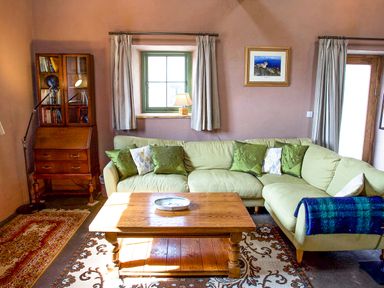 A living room with a green sectional sofa and a wooden coffee table by a window at Tyn Llwyn Cornel Eco Barn in Garreg