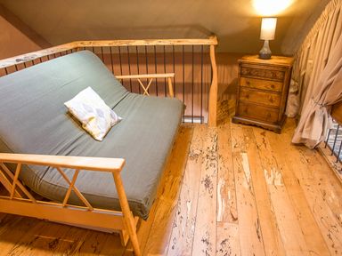 A wooden futon with a cushion beside a wooden nightstand with a lamp in a room at Tyn Llwyn Cornel Eco Barn in Garreg