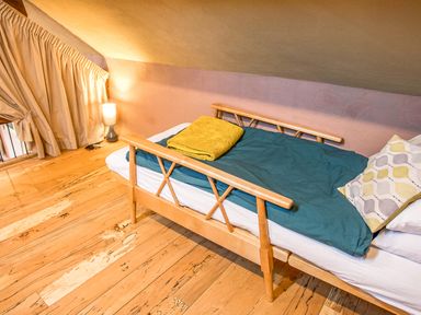 A small bedroom with a wooden bed with teal bedding and a yellow towel near a curtain and lamp at Tyn Llwyn Cornel Eco Barn in Garreg