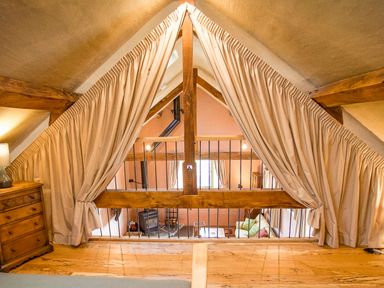 Attic space with wooden beams beige curtains and a chest of drawers overlooking a living area at Tyn Llwyn Cornel Eco Barn in Garreg