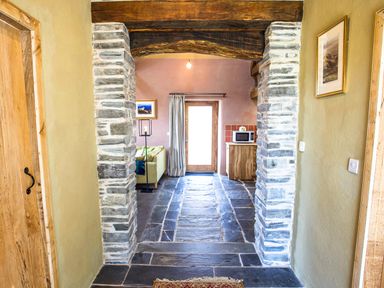 A hallway with stone pillars and slate flooring leading to a living area with a door curtain and microwave at Tyn Llwyn Cornel Eco Barn in Garreg
