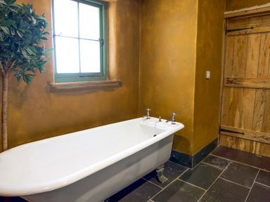 A bathroom with a window a white clawfoot bathtub a wooden door and a plant at Tyn Llwyn Cornel Eco Barn in Garreg
