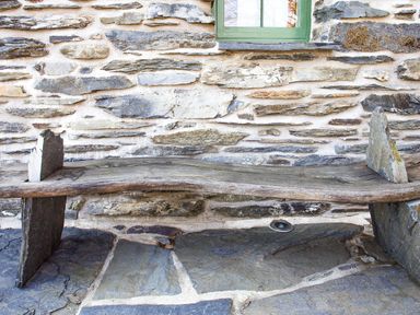 A wooden bench with stone supports against a stone wall under a green window at Tyn Llwyn Cornel Eco Barn in Garreg