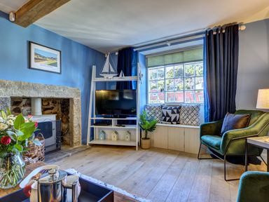 A living room with a stone fireplace a television on a white stand and a window seat with cushions at Crab Cottage in Sandsend