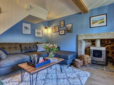 A living room with a blue sofa coffee table flowers fireplace and framed pictures on blue walls at Crab Cottage in Sandsend