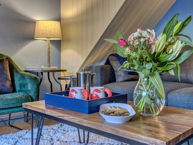 A living room with a wooden coffee table holding a vase of flowers mugs a teapot and a bowl of snacks at Crab Cottage Sandsend