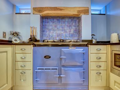 A kitchen with a blue stove set into a tiled alcove with wooden beam above at Crab Cottage in Sandsend