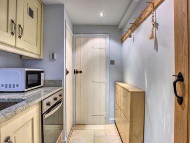 A kitchen area with a microwave on the counter an oven wooden cabinets a wooden coat rack and a wooden cabinet at Crab Cottage in Sandsend