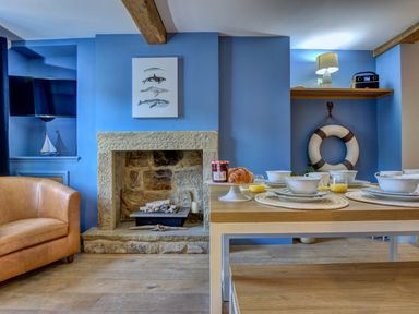 A dining area with a set table having plates and glasses next to a stone fireplace and a leather armchair at Crab Cottage in Sandsend