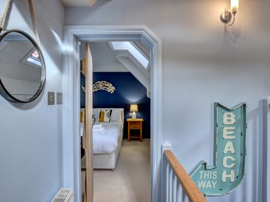 A hallway with a round mirror and a blue beach sign pointing to a bedroom in Crab Cottage Sandsend