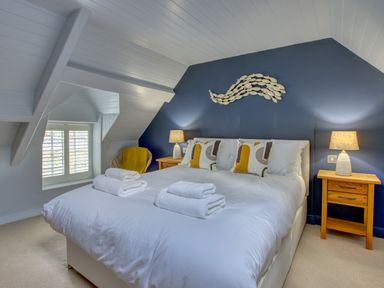 A bedroom with a double bed with white linens and folded towels bedside tables with lamps and a wicker chair at Crab Cottage in Sandsend