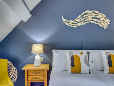 A bedroom with a bed with patterned pillows a wooden bedside table with a lamp a wicker chair and a fish-shaped wall decoration at Crab Cottage in Sandsend