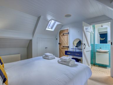 A bedroom with a white bed and folded towels with a wooden door a blue vanity table and an open door to a bathroom with turquoise tiles at Crab Cottage in Sandsend