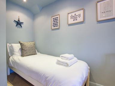 A single bed with white sheets and towels on top in a small bedroom with framed pictures on the wall at Crab Cottage in Sandsend