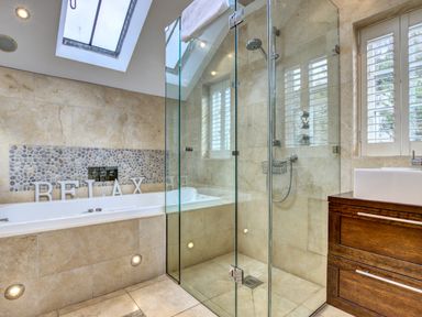 A bathroom with a tiled bathtub a glass shower enclosure a wooden vanity and a skylight at Crab Cottage in Sandsend