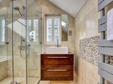 A bathroom with a glass shower enclosure a wooden vanity with a white sink and a towel radiator on a tiled wall at Crab Cottage in Sandsend