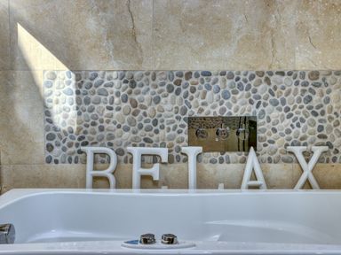 A bathroom with a white bathtub and pebble tile wall with letters spelling relax at Crab Cottage in Sandsend