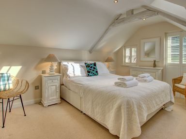 A bedroom with a double bed with white linens two bedside tables with lamps a wicker chair and a dresser with a mirror at Crab Cottage in Sandsend