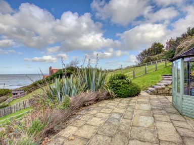 A coastal garden with tiled patio steps and a small gazebo near the sea at Crab Cottage in Sandsend