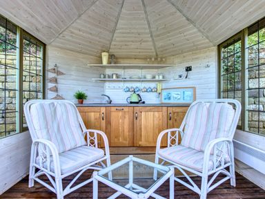 A small room with two cushioned chairs and a glass table facing a wooden cabinet with a sink and shelves at Crab Cottage in Sandsend