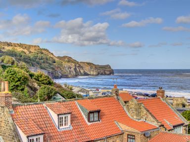 A coastal scene with red-roofed buildings in the foreground and cliffs by the sea in the background at Crab Cottage in Sandsend