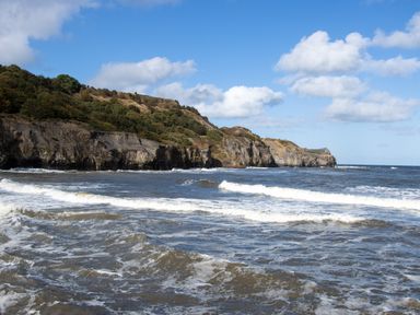 A coastal scene with waves and rocky cliffs under a partly cloudy sky at Crab Cottage in Sandsend