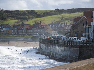 A coastal town with houses cars and people along a sea wall and beach at Crab Cottage in Sandsend