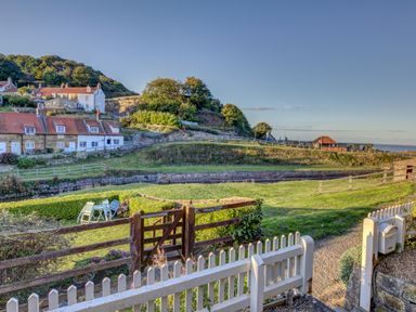 A garden with chairs and tables behind a wooden gate and fence near houses and a hill at Crab Cottage in Sandsend