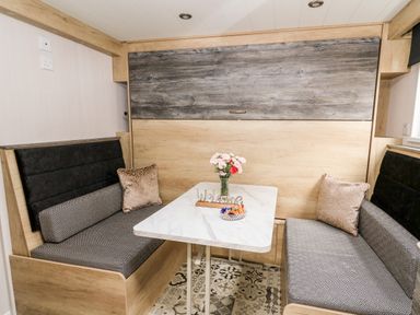 A dining area with a rectangular table flowers and a welcome sign on it and cushioned bench seats on either side at Oak Tree View in Nantmel near Rhayader