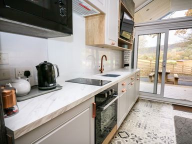 A kitchen with white cabinets a black oven a black microwave and a sliding glass door leading outside at Oak Tree View in Nantmel near Rhayader