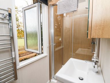 A bathroom with a sink a faucet a soap dispenser a shower with glass doors a towel rack and an open window at Oak Tree View Nantmel near Rhayader