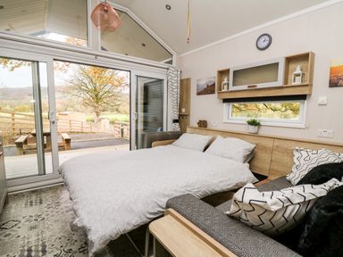 A bedroom with a bed a patterned sofa a window and sliding glass doors overlooking a fenced yard at Oak Tree View in Nantmel near Rhayader