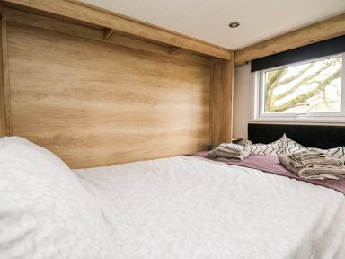 A bedroom with a bed covered in white sheets and folded towels on a purple runner near a window at Oak Tree View in Nantmel near Rhayader