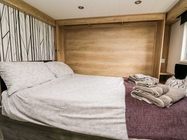 A bedroom with a bed made with light sheets and pillows and folded towels on a purple blanket at Oak Tree View in Nantmel near Rhayader