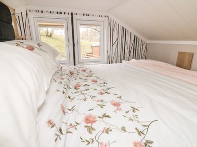 A bedroom with a bed covered in floral patterned bedding under two windows at Oak Tree View in Nantmel near Rhayader
