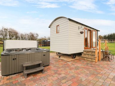 An outdoor area with a hot tub and a small building with wooden steps and chairs at Highland View in Rhayader