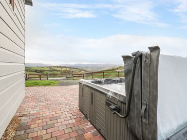An outdoor hot tub on a brick patio next to a building with a view of rolling hills and fields at Highland View in Rhayader