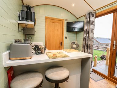 A small kitchen area with a countertop, two stools, a toaster, a knife block, a wall-mounted TV, and a door leading outside at Highland View in Rhayader