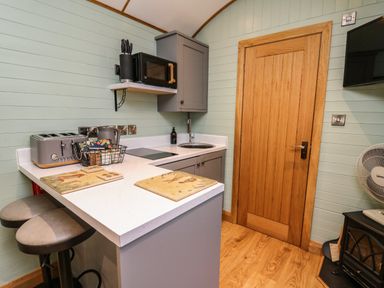A small kitchen with a wooden door a countertop with two stools microwave toaster and a fan at Highland View in Rhayader