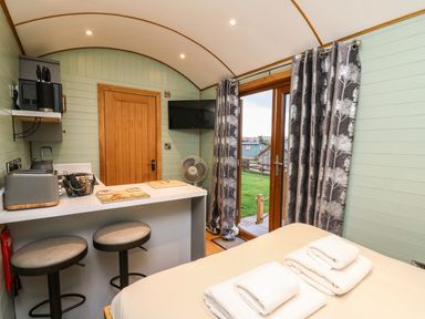 A small kitchen and bedroom area with a breakfast bar stools and towels on bed at Highland View in Rhayader