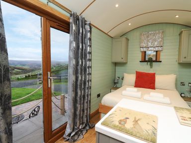 A bedroom with a double bed and folded towels next to a glass door with curtains at Highland View in Rhayader