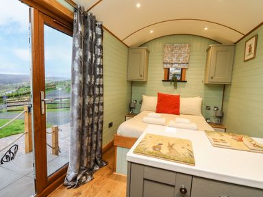 A compact bedroom with a bed pillows and towels next to a window and sliding glass door at Highland View in Rhayader