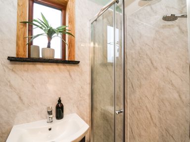 A bathroom with a sink, soap dispenser, shower enclosure, window with wooden frame, and a plant on the windowsill at Highland View in Rhayader